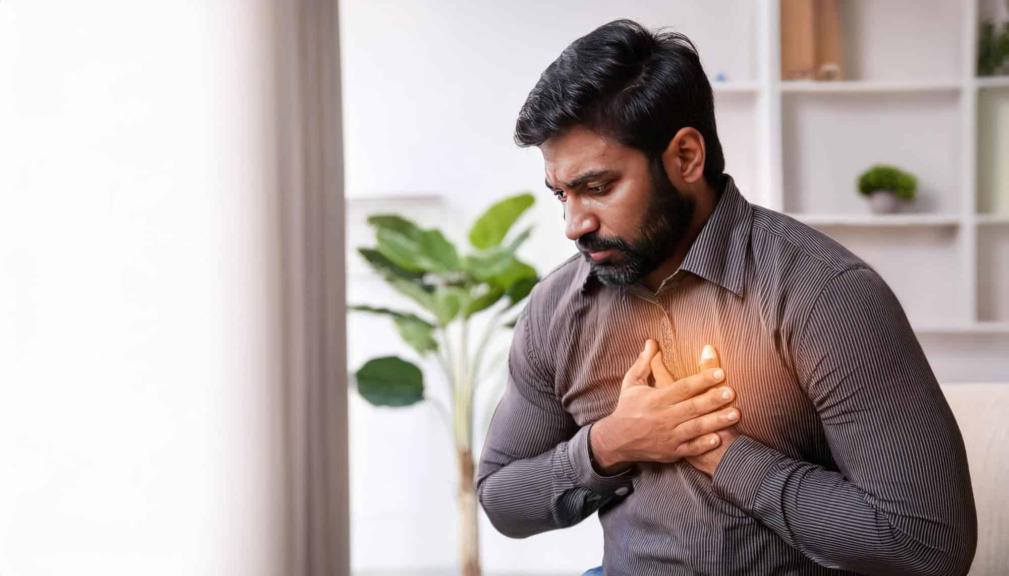 A man with a beard holds his chest with both hands, looking down with a pained expression.
